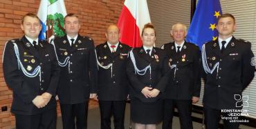 Sala, obok siebie w rzędzie stoi sześciu strażaków (w tym jedna kobieta). Ubrani są w stroje galowe.