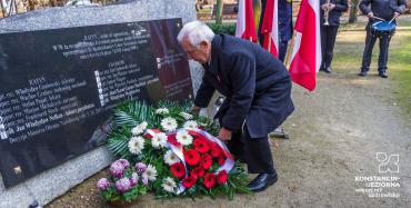 Park. Mężczyzna w średnim wieku składa wieniec z biało-czerwonymi kwiatami przed pomnikiem Pamięci Ofiar Katynia. 