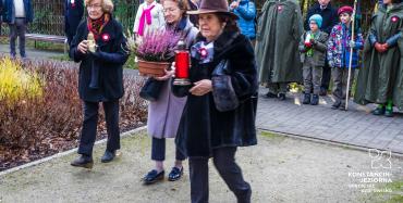 Park. Trzy seniorki idą złożyć kwiaty i znicze przed pomnikiem Pamięci Ofiar Katynia.