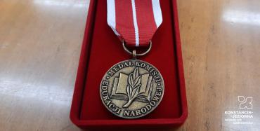 W czerwonym etui leży medal, który ma kształt koła. Wykonany jest z metalu koloru jasnobrązowego. Na nim widnieje wizerunek otwartej książki przełożonej gałązką drzewa laurowego oraz napis w Medal Komisji Edukacji Narodowej.