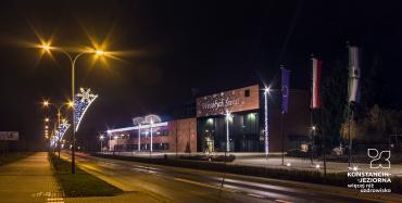 Ulica nocą. Po lewej stronie widoczne są latarnie, na których zamontowano zwisające ozdoby świąteczne.