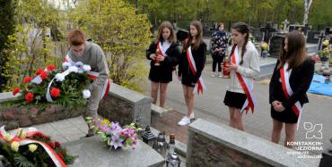 Delegacja uczniów w biało czerwonych szarfach składający kwiaty na pomniku. 