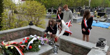 Delegacja uczniów w biało czerwonych szarfach składający kwiaty na pomniku. 