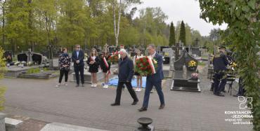Drugi zastępca burmistrza niosący kwiaty w stronę pomnika, obok przewodniczący koła nr 21 Polskiego Związku Emerytów, Rencistów i Inwalidów w Konstancinie-Jeziornie. W tle uczniowie i nauczyciele. 