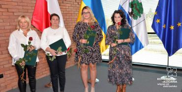 Cztery kobiety stoją obok siebie w rękach trzymają duże róże i dyplomy. 