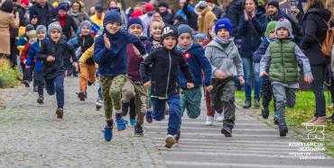 8.	Dzieci biegną chodnikiem w parku, przy chodniku stoją rodzice i robią zdjęcia.