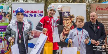 9.	Trzech chłopców w strojach sportowych,  z pucharami  w rękach i medalami na szyi. Za nimi stoi mężczyzna.