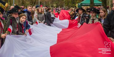 Tłum młodzieży i dzieci w parku, którzy trzymają 100-metrową biało-czerwona flagę.
