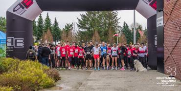 Mężczyźni i kobiety w strojach sportowych czekają  w bramce startowej na rozpoczęcie biegu.