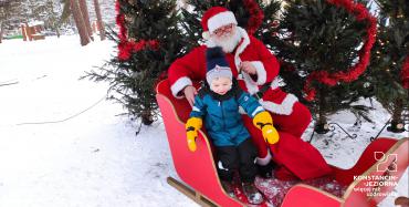 Święty Mikołaj z dzieckim w , do których są zaprzęgnięte dwa renifery.