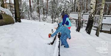 Na zdjęciu śnieg, dwie dziewczynki kłada znicz na mogile.