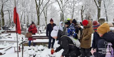 Dzieci kłada znicz na grobie. Przy grobie wbita jest biało czerwona flaga.