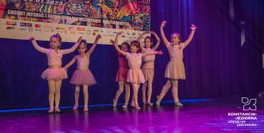Dziewczynki w strojach baletnic tańczą na scenie. Mają rączki uniesione do góry.