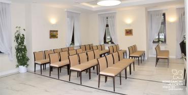 Wnętrze sali ślubów w willi Kamilin. Kremowe ściany, rzędy jasnych krzeseł. 