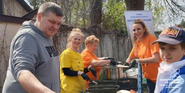 Grill, przy którym stoji mężczyzna i trzy kobiety. Na grilu pieka się kiełbaski. Za nimi baner z napisem: Zadanie realizowane w ramach inicjatywy lokalnej.