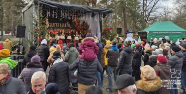 Występ lokalnych zespołów i chórów na scenie, z widocznymi świątecznymi dekoracjami i oświetleniem.