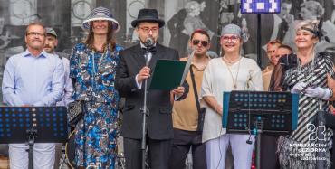 Burmistrz Michał Wiśniewski w stroju z epoki przemawia ze sceny w otoczeniu uczestników Pikniku Retro.