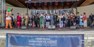 Grupa uczestników Pikniku Retro stoi na scenie amfiteatru podczas wspólnej prezentacji.