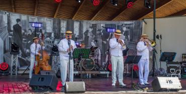 Zespół muzyczny w białych strojach wykonuje koncert jazzowy na scenie amfiteatru.