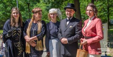 Uczestnicy Pikniku Retro pozują do wspólnego zdjęcia w strojach inspirowanych latami 20. i 30. XX wieku.