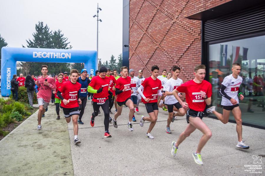 A  large group of young people dressed in white and red outfits starting to run, fragments of a large red brick building visible on the right 