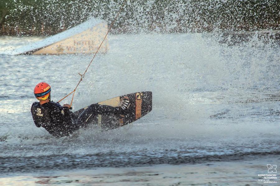 A man on a water ski, holding a line that pulls him in the water, the waves are splashing 