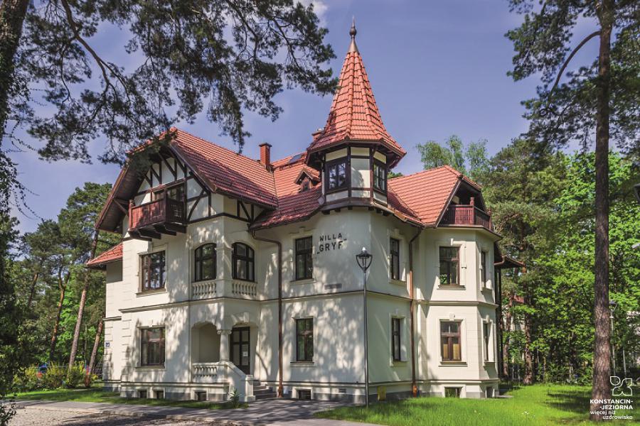 A historic two-story building with a sloping tiled roof, visible formwork, around a tree 