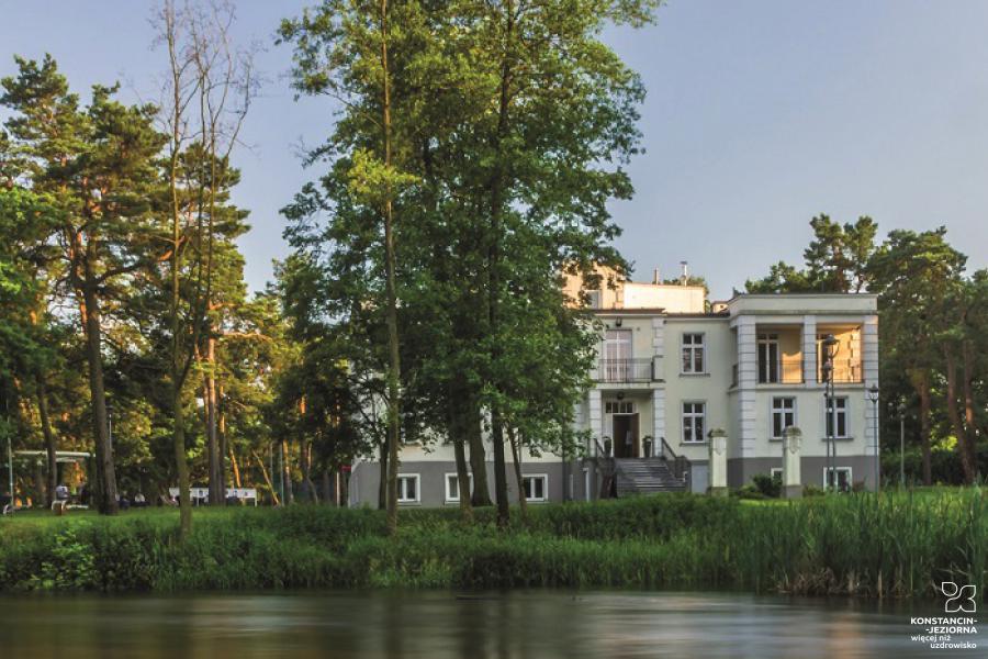 A two-story building by the water, around a tree. 