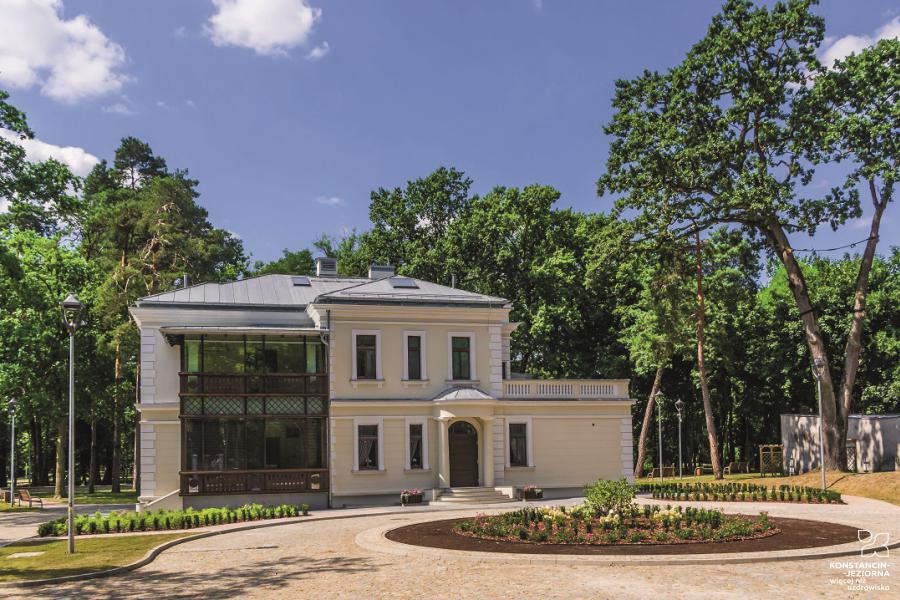 A two-story building with white walls and a wooden veranda stands among the trees