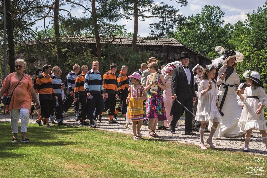 A group of people in costumes from the beginning of the 20th century marches against the background of the graduation towers in the Park 