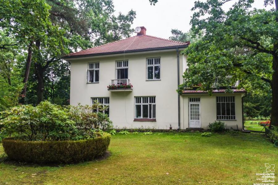 A two-story house with a sloping roof, situated around trees 