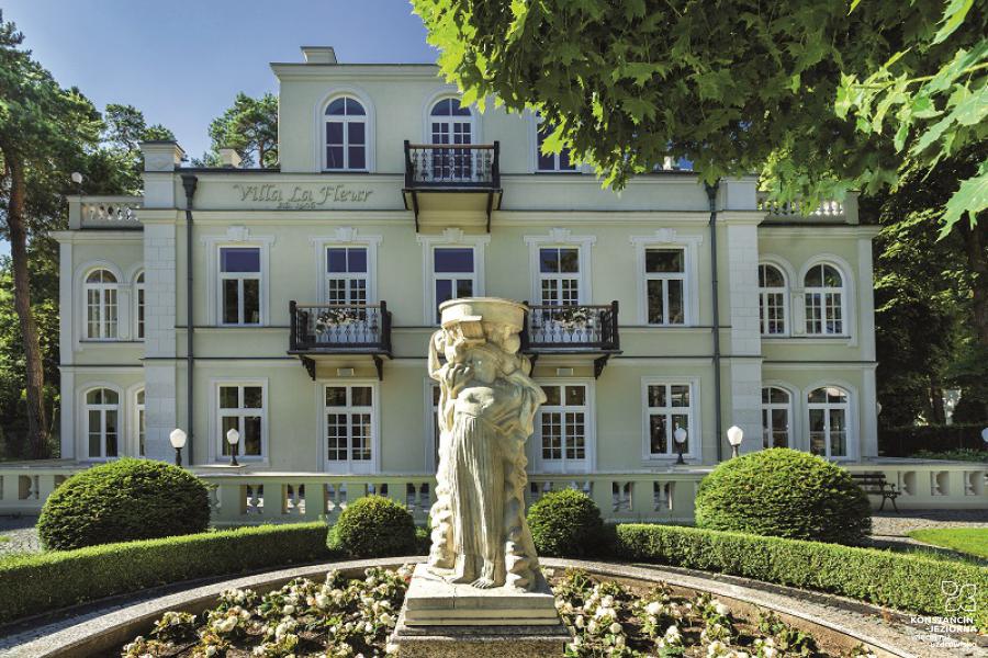 An elegant two-story villa in the style of the French Empire, a sculpture stands in front of the flower bed 