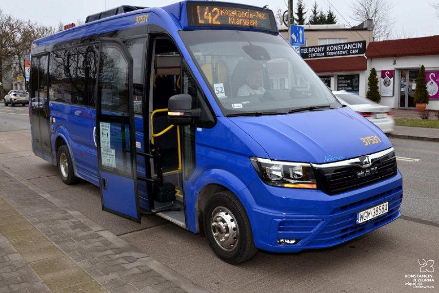 Niebieski bus stoi na przystanku, ma otwarte boczne drzwi, nad przednią szybą wyświetlacz z numerem linii L42 i nazwami przystanków – początkowego Konstancin-Jez. i końcowego – Klarysew.