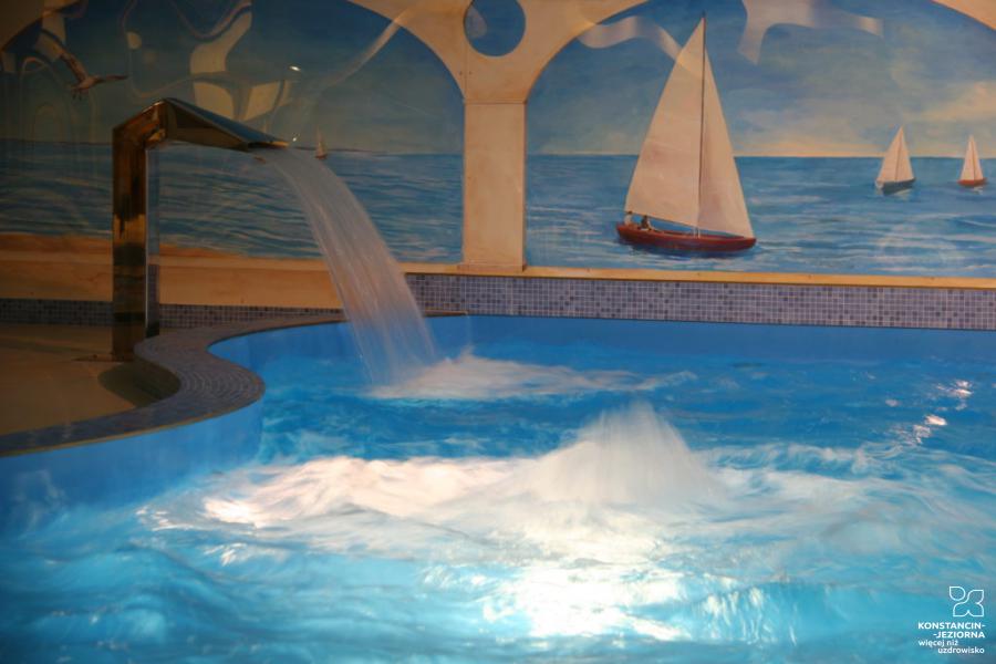 The interior of the swimming pool in the building, colorful maritime theme graphics on the walls, on the left side of the pool water is poured from a pipe 