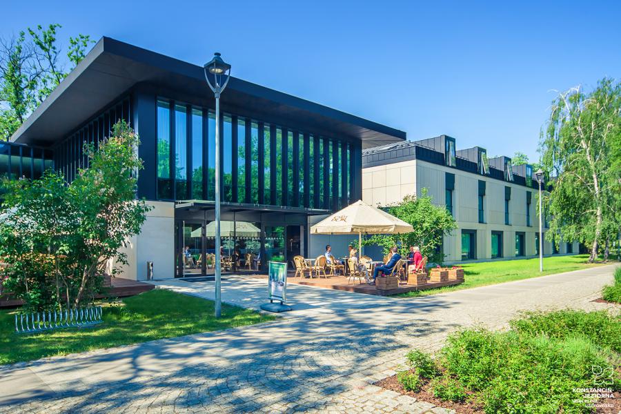 On the left, a modern building with large glass walls, a park path in front of it, around a tree 