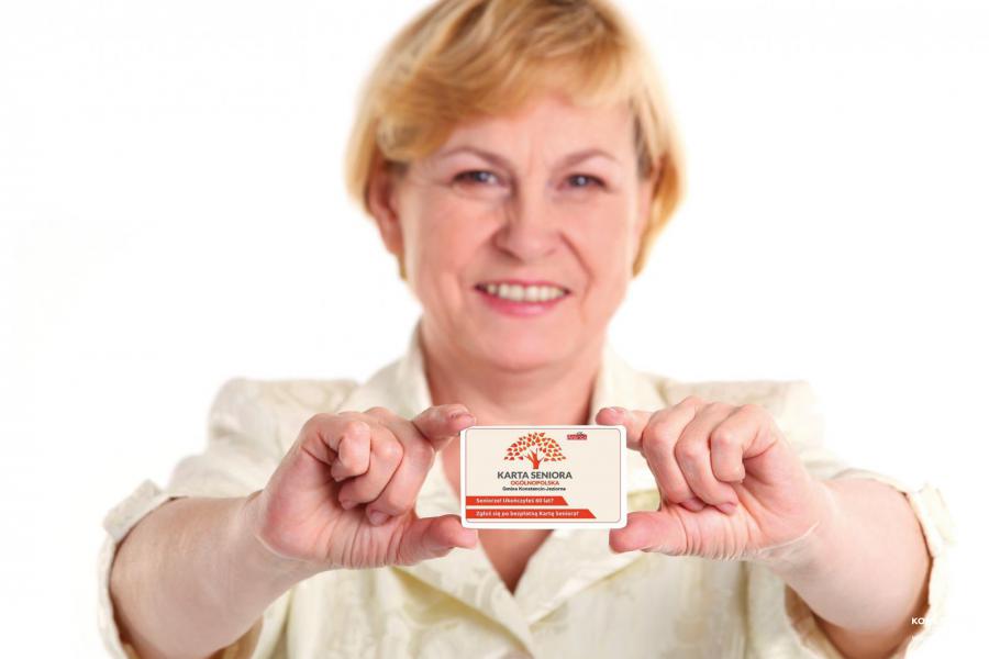 Na zdjęciu uśmiechnięta seniorka, która w rękach trzyma Konstancińską Kartę Seniora.