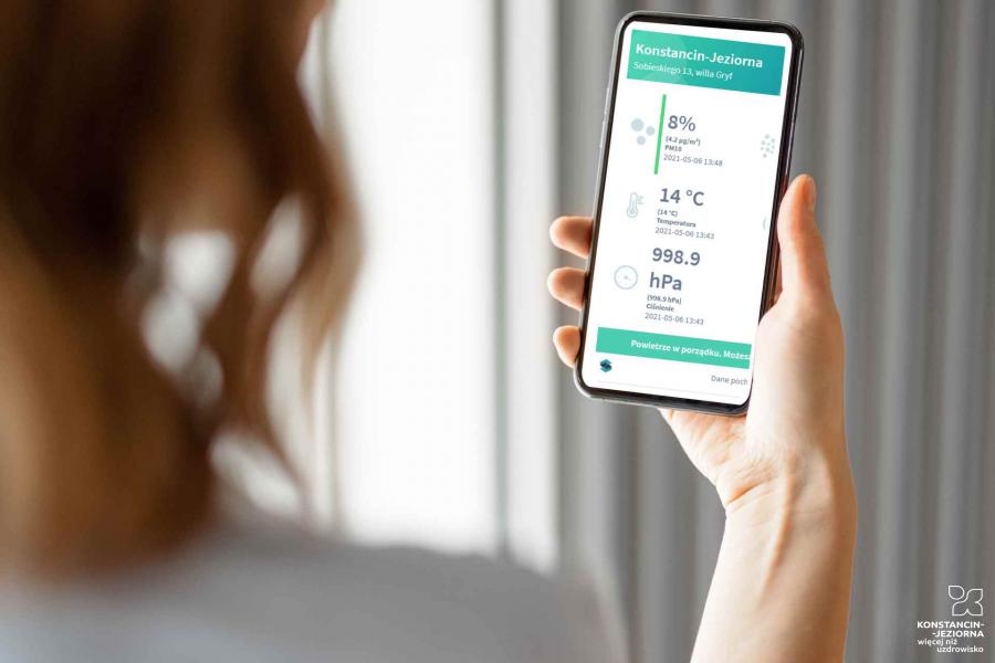 Kobieta trzymająca telefon komórkowy i sprawdzająca jakość powietrza w aplikacji mobilnej.