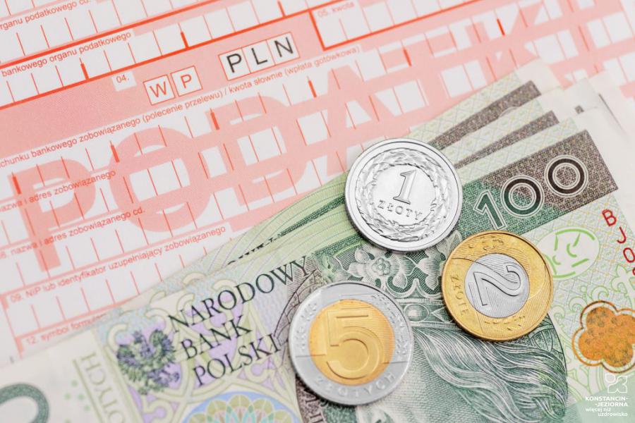 Na bloczku pocztowym do płacenia podatków ułożone banknoty o nominale stu złotych oraz monety o nominale 1 złoty, 2 złote i 5 złotych. 