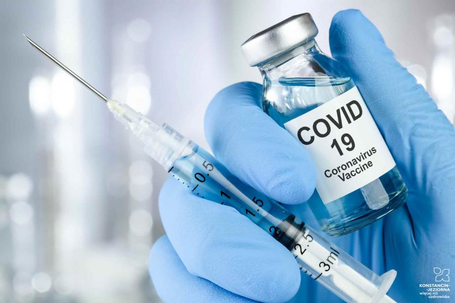 Dłoń w niebieskiej rękawiczce trzymająca strzykawkę i buteleczkę z napisem COVID-19 Coronavirus Vaccine.