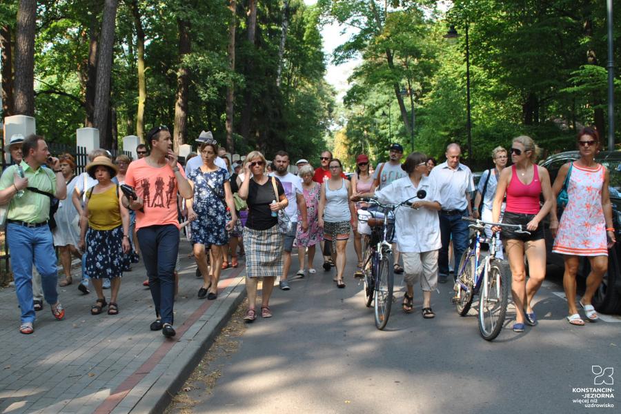 Grupa około 30 osób, która idzie całą szerokością ulicy. W tle widać wysokie drzewa.