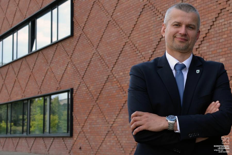 Uśmięchnięty mężczyzna na tle budynku z czerwonej cegły.