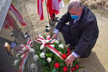 Mężczyzna przyklęka przed tablicą na pomniku, składa wiązankę ozdobioną biało-czerwonymi kwiatami