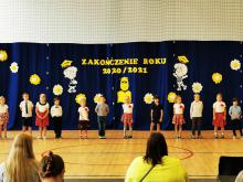 Grupa dzieci na Sali gimnastycznej podczas przedstawienia na zakończenie roku szkolnego, na pierwszym planie publiczność. 