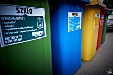 Zdjęcie przedstawia pięć dużych pojemników na śmieci segregowane. Ustawione są obok siebie, różnią się kolorami (od lewej: zielony, niebieski, żółty, czerwony, zielony).