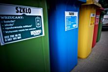 Pięć dużych pojemników na śmieci segregowane. Ustawione są obok siebie, różnią się kolorami (od lewej: zielony, niebieski, żółty, czerwony, zielony).