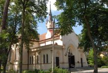 Budynek kościoła parafialnego z portalem, nawą główną, wieżą i czerwoną dachówką w otoczeniu drzew.