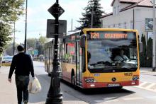 Ulica, po której jedzie czerwono-pomarańczowy autobus komunikacji miejskiej. Nad jego przednią szybą wyświetla się napis: 724 Metro Kabaty.