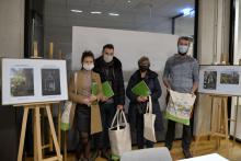 Sala konferencyjna. Cztery osoby w maseczkach stoją przodem i trzymają w rękach torby płócienne oraz zielone teczki na dokumenty.