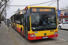 Ulica, po której jedzie czerwono-pomarańczowy autobus komunikacji miejskiej. Nad jego przednią szybą wyświetla się napis: 710 Osiedle Kabaty.