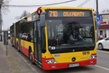 Ulica, po której jedzie czerwono-pomarańczowy autobus komunikacji miejskiej. Nad jego przednią szybą wyświetla się napis: 710 Osiedle Kabaty.